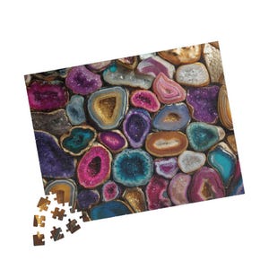 May include: A colorful jigsaw puzzle featuring a close-up of various geode slices. The puzzle pieces display a variety of colors, including pink, purple, blue, and gold, creating a vibrant and eye-catching design. Some puzzle pieces are separate.