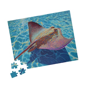 May include: A completed jigsaw puzzle featuring a vibrant illustration of a stingray swimming in blue water. The stingray has a patterned design in shades of orange, brown, and purple. Several puzzle pieces are separate from the completed puzzle.