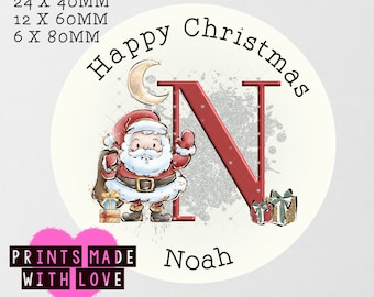 May include: A round, white sticker with a red and white Santa Claus illustration, a silver glitter background, and the letter N in red. The sticker also includes the text "Happy Christmas" and "Noah".