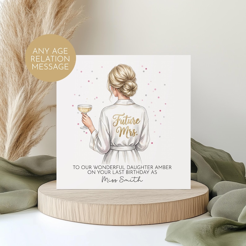 May include: A greeting card featuring an illustration of a woman in a white robe holding a champagne glass. The robe has "Future Mrs." in gold script. The card includes text: "TO OUR WONDERFUL DAUGHTER AMBER ON YOUR LAST BIRTHDAY AS Miss Smith."