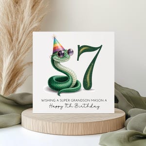 May include: A birthday card with a green snake wearing sunglasses and a party hat. The number 7 is next to the snake. The text reads, "Wishing a super grandson Mason a Happy 7th Birthday."