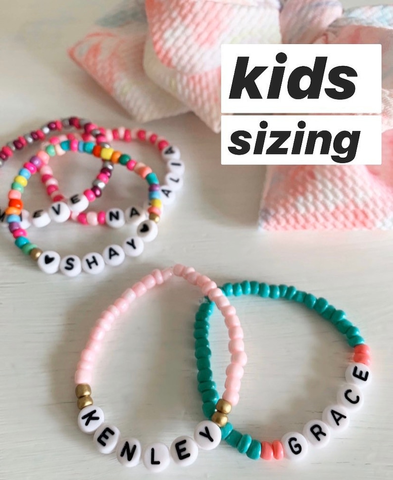 May include: Colorful beaded bracelets with personalized names, including "Shay", "Ali", "Kenley", and "Grace". The bracelets are made with small, colorful beads and white letter beads. The image includes the text "kids sizing".
