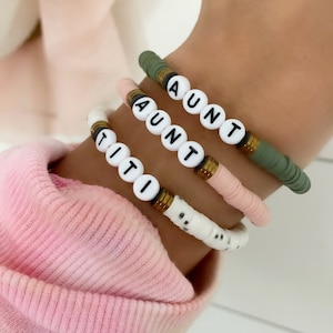 May include: Three beaded bracelets with the words "AUNT" spelled out on each. The bracelets are in green, pink and white.
