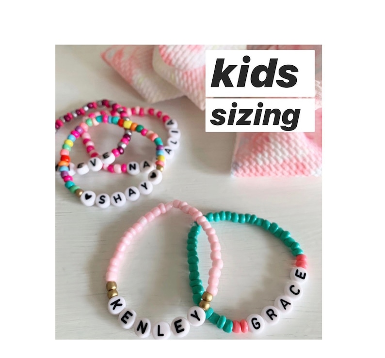 May include: Four colorful beaded bracelets with different names spelled out on them. The bracelets are pink, turquoise, and rainbow colors. The text "kids sizing" is written in black on a pink and white background.