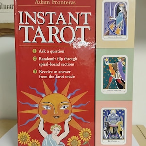 May include: A red book titled "INSTANT TAROT" by Adam Fronteras, with instructions and sample tarot cards. The cover features a sun graphic and the text "Ask a question, Randomly flip through spiral-bound sections, Receive an answer from the Tarot oracle."