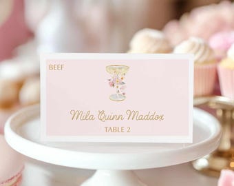 Puede incluir: Tarjeta de lugar rosa con letras doradas. La tarjeta tiene una ilustración floral y el texto "BEEF", "Mila Quinn Maddox" y "TABLE 2".
