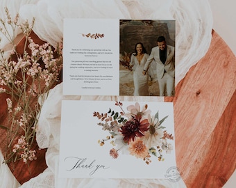May include: A thank you card featuring a floral design in shades of pink, red, and orange. The card has the text "Thank you" in elegant calligraphy. The card is on a wooden surface with a white fabric background. The card also includes a photograph of a couple in a desert setting.