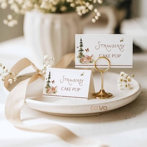 K&ouml;nnte beinhalten: Zwei wei&szlig;e Tischkarten mit dem Text "Strawberry Cake Pop" und einer Aquarellillustration eines Rehs, Schmetterlingen und eines Baumes. Ein goldfarbener Metall-Kartenhalter h&auml;lt eine Karte. Die Karten liegen auf einem wei&szlig;en Teller.
