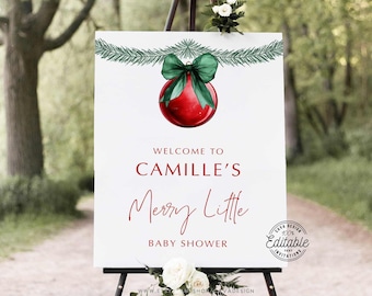 May include: A white welcome sign with green pine branches and a red Christmas bauble with a green bow. The sign reads "Welcome to Camille's Merry Little Baby Shower".