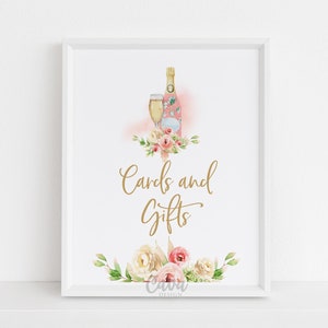 May include: A white frame with a sign that says "Cards and Gifts" in gold lettering. The sign is decorated with watercolor flowers and a champagne bottle and glass.