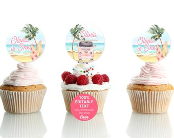 May include: Three pink and white cupcakes with pink frosting and sprinkles. Each cupcake has a round, pink and blue paper topper with a beach scene, palm trees, a surfboard, and a pink van with the text "Olivia is One".