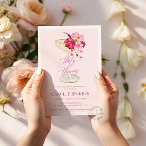 May include: Pink and white birthday party invitation with a champagne flute illustration and floral accents. The text reads "thirty & thriving" and includes the party details: date, time, location, and RSVP information.
