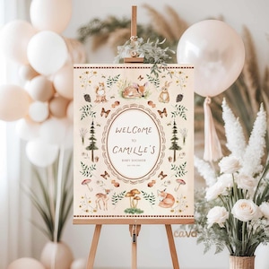 K&ouml;nnte beinhalten: Ein Willkommensschild f&uuml;r eine Babyparty auf einer Staffelei. Das Schild zeigt ein Waldthema mit Illustrationen eines Fuchses, eines Rehs, eines Kaninchens und eines Eichh&ouml;rnchens. Der Text lautet "Willkommen zu Camilles Babyparty". Das Schild ist von Ballons und Blumengestecken umgeben.