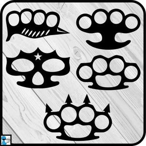 May include: Five black metal knuckle dusters with different designs. The knuckle dusters are on a white wood background.