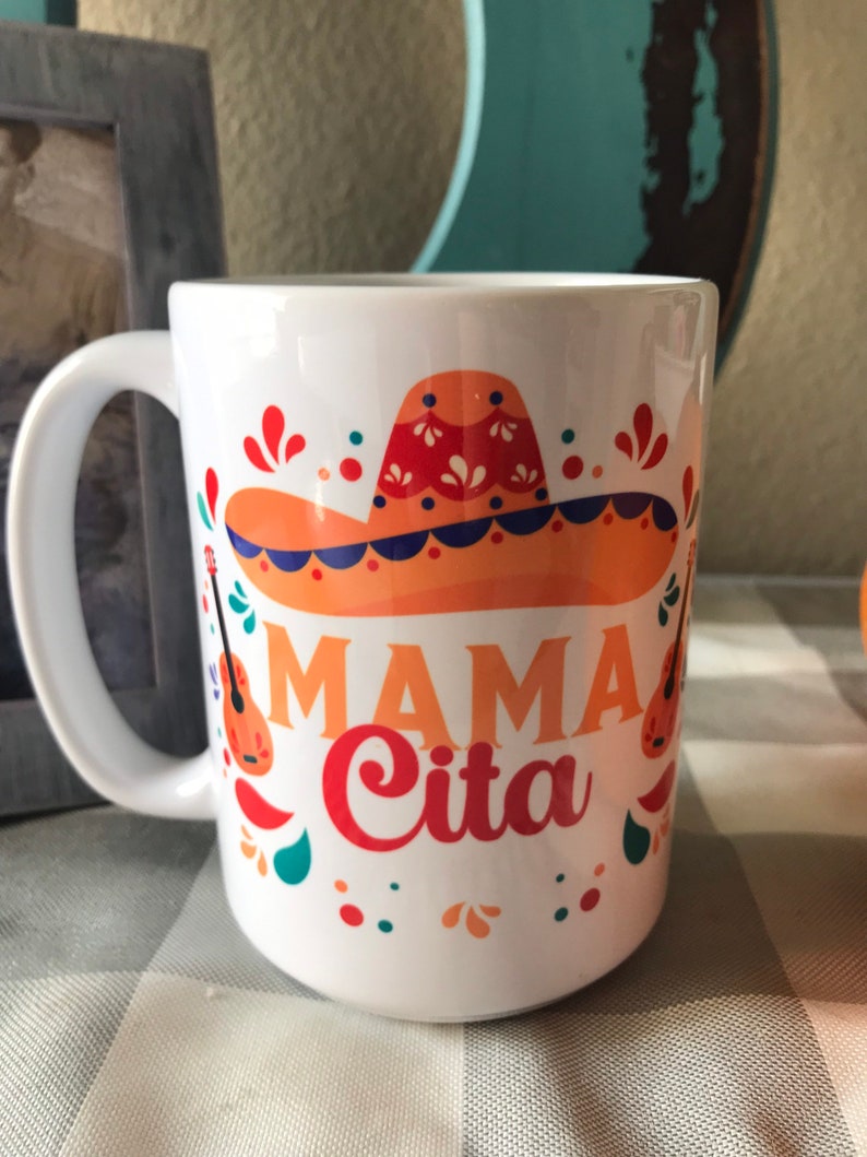 May include: White ceramic mug with a colorful design featuring a sombrero, guitars, and the text "Mama Cita".