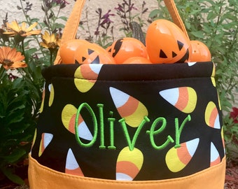 May include: Black and orange Halloween trick-or-treat bag with a candy corn pattern and the name "Oliver" embroidered in green. The bag is filled with orange plastic pumpkin-shaped candy holders.