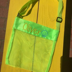May include: A lime green mesh beach bag with a satin top flap. The bag has a black adjustable strap and is embroidered with the name "Oliver" and a seashell.