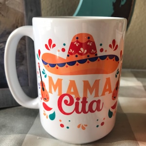 May include: White ceramic mug with a colorful design featuring a sombrero, musical instruments, and the text "Mama Cita".