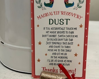 May include: A small, red and white card with a cartoon elf's legs and the words "Magical Elf Recovery Dust". The card has instructions for how to use the magic dust to revive a tired elf. A small glass bottle with gold glitter and a wooden tag that says "Magic Elf Dust" is attached to the card with a red ribbon.