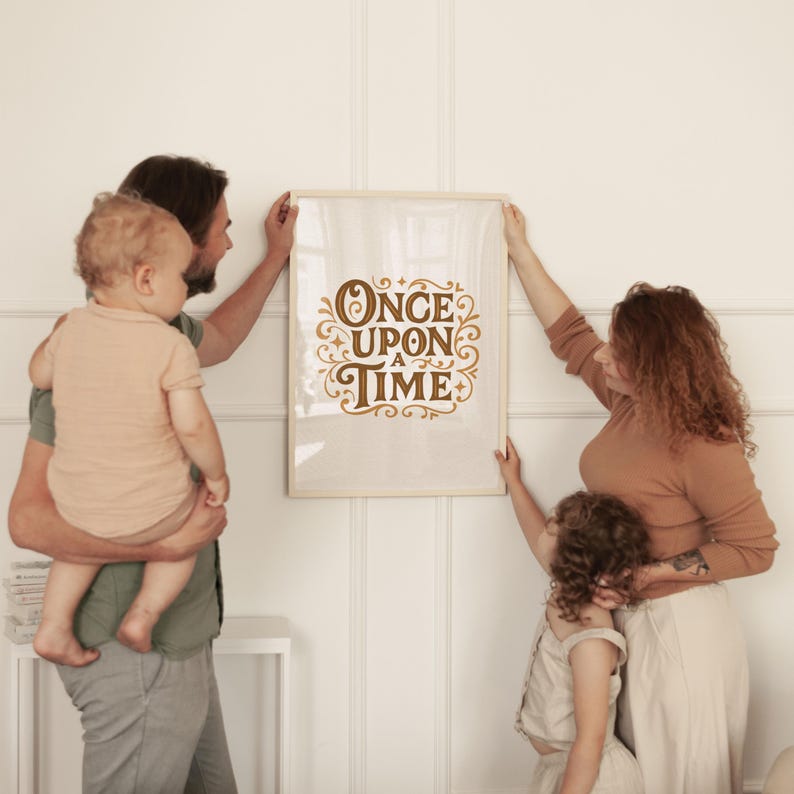 May include: A framed print with the words "ONCE UPON A TIME" in a decorative brown font. The print is being held by a family in front of a white wall. The print has a light beige background.