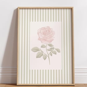 K&ouml;nnte beinhalten: Ein gerahmter Kunstdruck mit einer zarten rosa Rose mit gr&uuml;nen Bl&auml;ttern und Stiel. Das Kunstwerk ist vor einem hellrosa Hintergrund platziert und von einem hellgr&uuml;nen und wei&szlig;en gestreiften Rahmen umgeben, der in einem Holzrahmen eingefasst ist.
