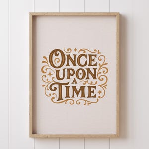 May include: A framed print with the words "ONCE UPON A TIME" in a decorative, vintage-style font. The text is in a warm brown color and is surrounded by ornate flourishes. The frame is a light wood color, and the background is a neutral off-white.