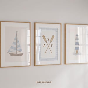 May include: Three framed prints with a nautical theme. The left print features a sailboat with blue and white stripes. The center print has a blue and white gingham pattern with two crossed oars and the letters "SAF". The right print shows a lighthouse with blue and white stripes.