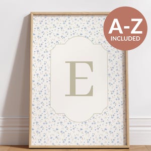 May include: Framed wall art featuring a floral pattern with small blue flowers on a cream background. The artwork includes a central design with the letter "E" in a light green color. The text "A-Z INCLUDED" is in a circle in the upper right corner.