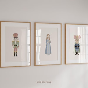 May include: Three framed art prints featuring watercolor illustrations. The prints depict a nutcracker, a princess in a blue dress, and a mouse in a cape. The frames are a light brown color, and the background is a neutral tone.