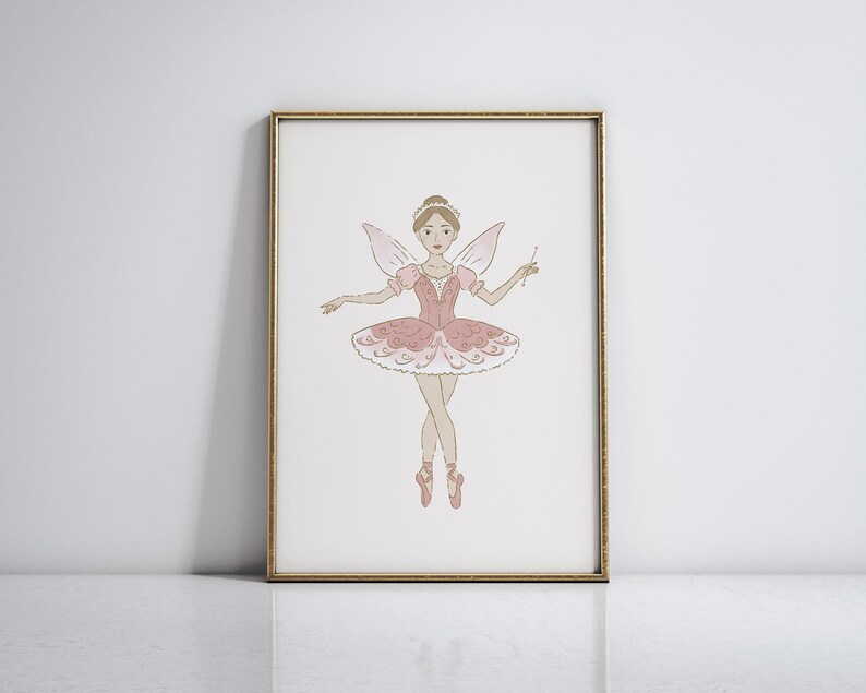 May include: A framed print featuring a whimsical illustration of a ballerina fairy. The fairy is depicted in a pink tutu, wings, and pointe shoes, holding a wand. The artwork is set against a white background, framed in gold.