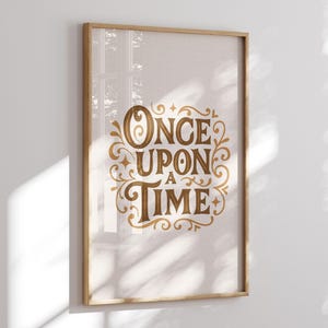 May include: A framed print with the words "ONCE UPON A TIME" in elegant gold script. The text is surrounded by decorative flourishes on a light beige background. The frame is made of light-colored wood.