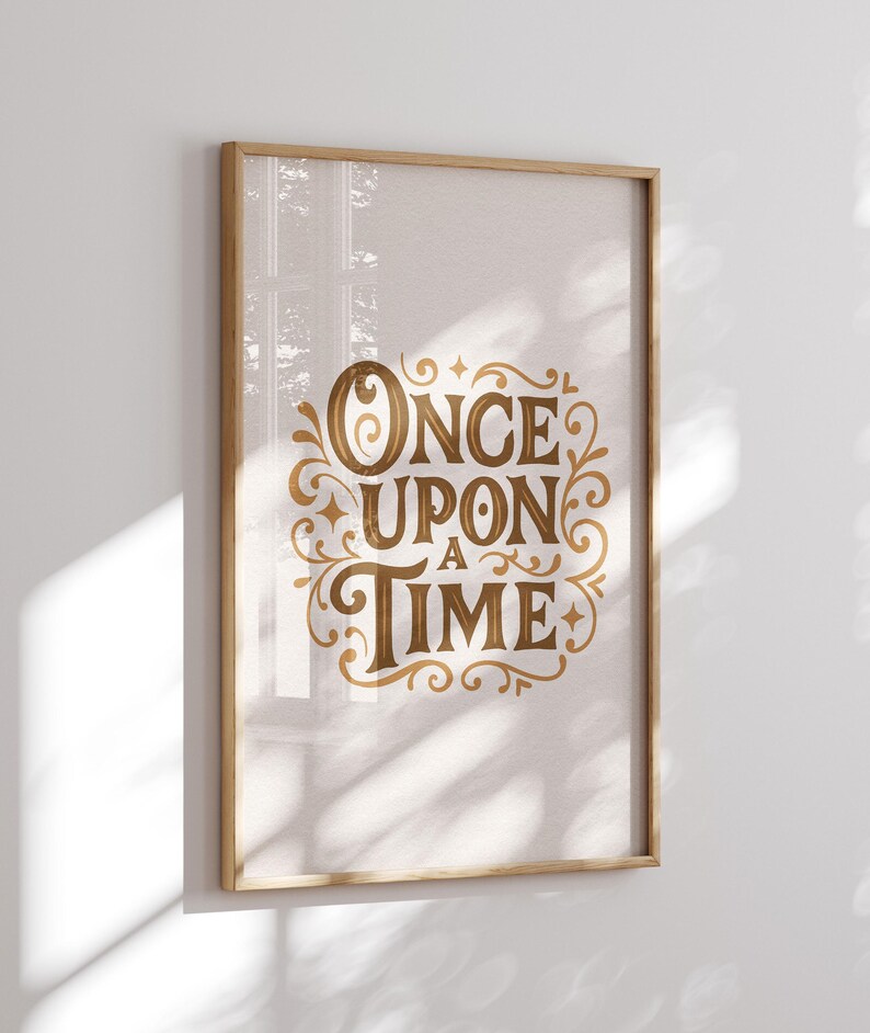 May include: A framed print with the words "ONCE UPON A TIME" in elegant gold script. The text is surrounded by decorative flourishes on a light beige background. The frame is made of light-colored wood.