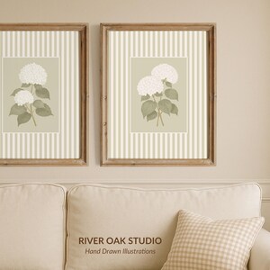 May include: Two framed floral prints featuring white hydrangea blooms on a light green background with a striped pattern. The frames are a warm brown color, and the prints are displayed above a cream-colored sofa.