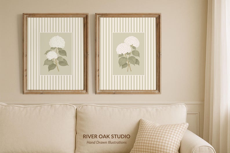 May include: Two framed floral prints featuring white hydrangea blooms on a light green background with a striped pattern. The frames are a warm brown color, and the prints are displayed above a cream-colored sofa.