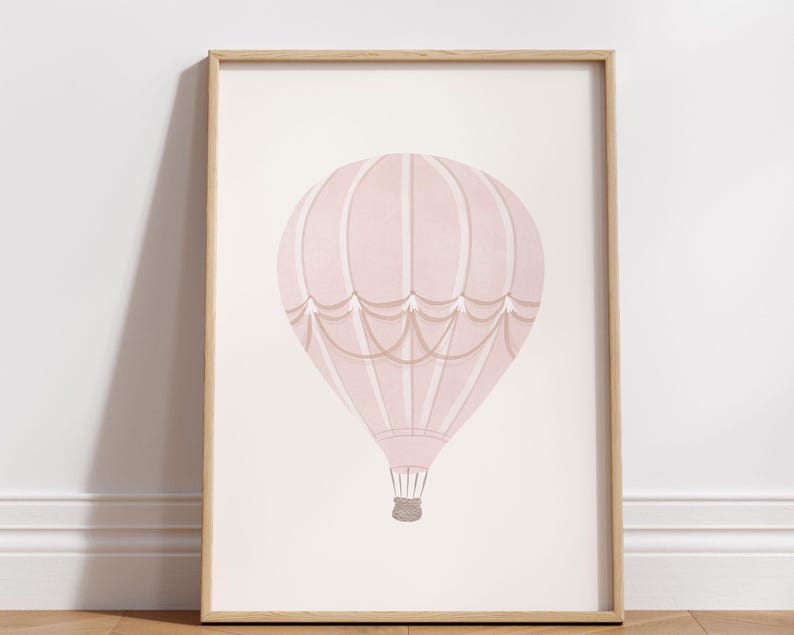 May include: A framed print featuring a pink hot air balloon illustration. The balloon has a striped design with tan accents and a woven basket. The artwork is set against a light background, framed in natural wood.