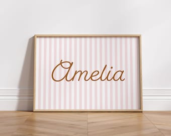 May include: A framed print with a pink and white striped background and the name "Amelia" written in brown cursive.
