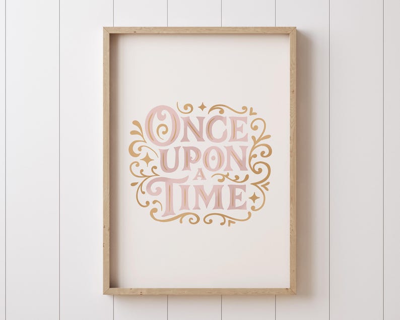 May include: A framed print with the words "ONCE UPON A TIME" in pink and gold script. The text is surrounded by decorative flourishes and set against a cream background. The frame is a light wood color.