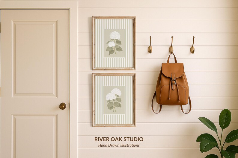 May include: Two framed botanical prints with white flowers and green leaves hang on a cream-colored wall. A brown leather backpack hangs from a hook. The text "RIVER OAK STUDIO Hand Drawn Illustrations" is at the bottom.