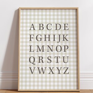 May include: A framed alphabet print. The print features the letters A through Z in a dark gray font, arranged on a light beige and white gingham pattern background. The frame is a light wood color.