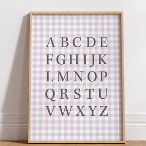 May include: A framed alphabet print featuring a lavender and white gingham pattern background. The letters A through Z are displayed in a dark gray font. The wooden frame adds a classic touch to this educational wall art.