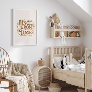 May include: A framed print with the words "Once Upon a Time" in gold script hangs on a white wall. The room features a wooden bed, a woven chair, and a woven side table. A cream-colored blanket is draped over the chair.