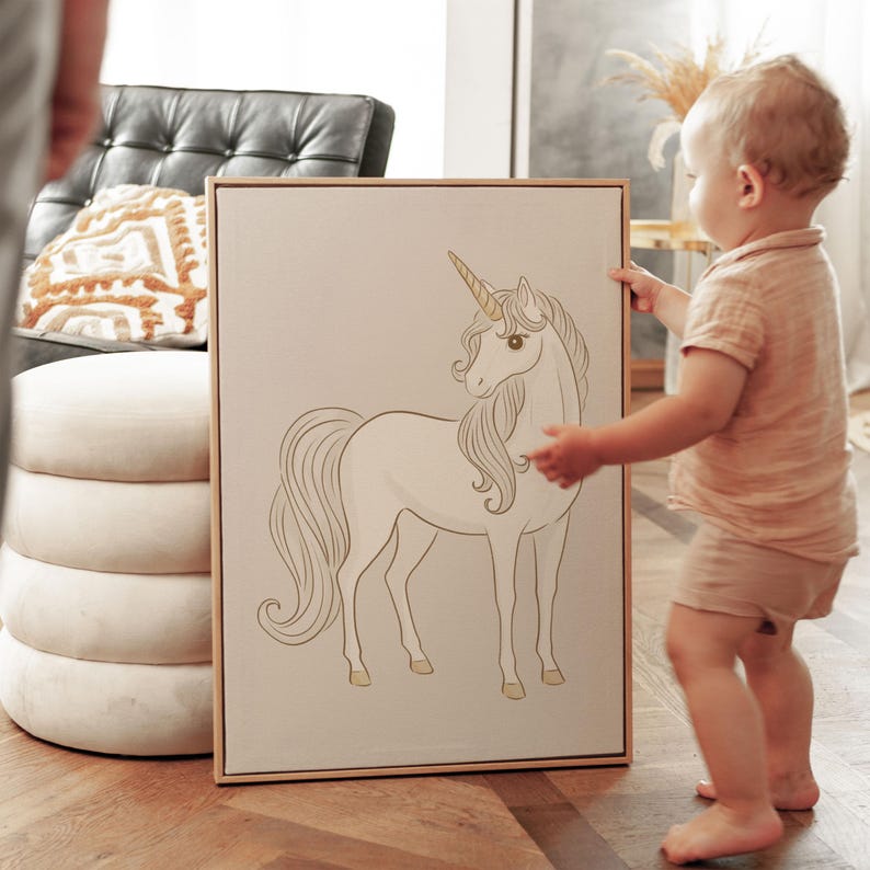 May include: A framed canvas art print featuring a white unicorn with a golden horn and hooves. The unicorn is depicted in a graceful pose against a neutral background. The artwork is displayed in a light-colored wooden frame, suitable for a nursery or children's room.