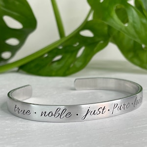 May include: Silver bracelet with the inscription "true · noble · just · pure · love" engraved on it.