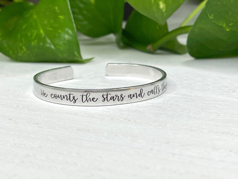 May include: A silver bracelet with the inscription "He counts the stars and calls them by name."