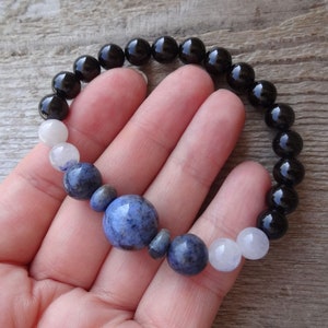 Op de afbeelding: Een armband met zwarte, witte en blauwe kralen. De armband heeft een grotere blauwe kraal in het midden.
