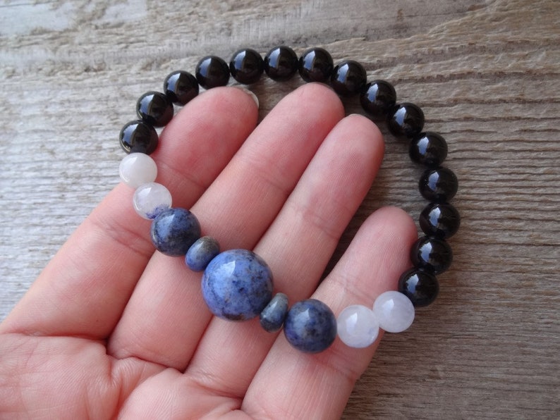 Op de afbeelding: Een armband met zwarte, witte en blauwe kralen. De armband heeft een grotere blauwe kraal in het midden.