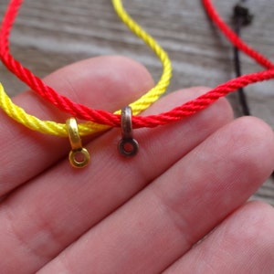 May include: Two cords of red and yellow string with gold and bronze metal clasps. The cords are tied together and held in a hand.