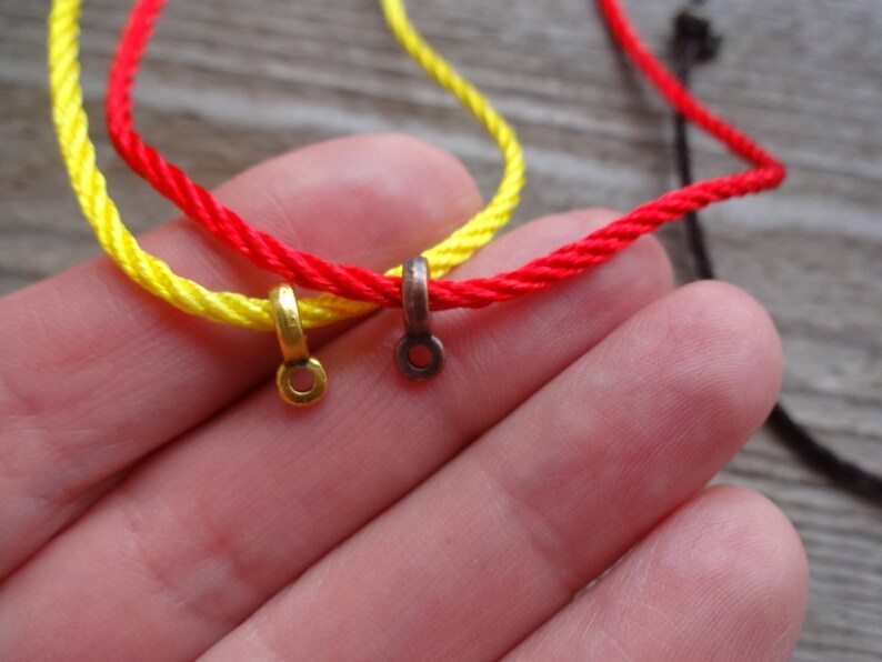 May include: Two cords of red and yellow string with gold and bronze metal clasps. The cords are tied together and held in a hand.