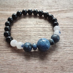 Op de afbeelding: Een armband met zwarte, witte en blauwe kralen met een grote blauwe steen in het midden.