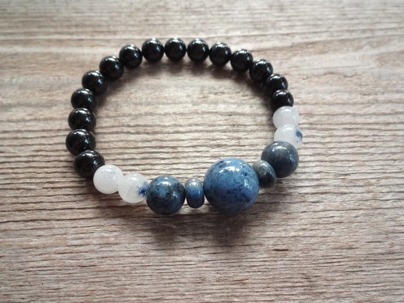 Op de afbeelding: Een armband met zwarte, witte en blauwe kralen met een grote blauwe steen in het midden.